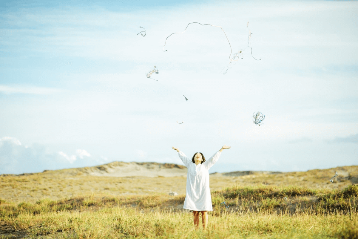 女性が草原で両腕を空に広げている画像